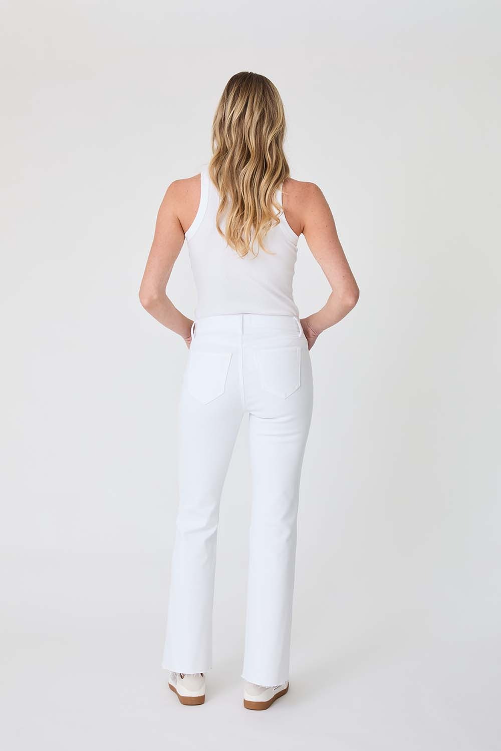 Woman wearing a white sleeveless top and pants on a plain background