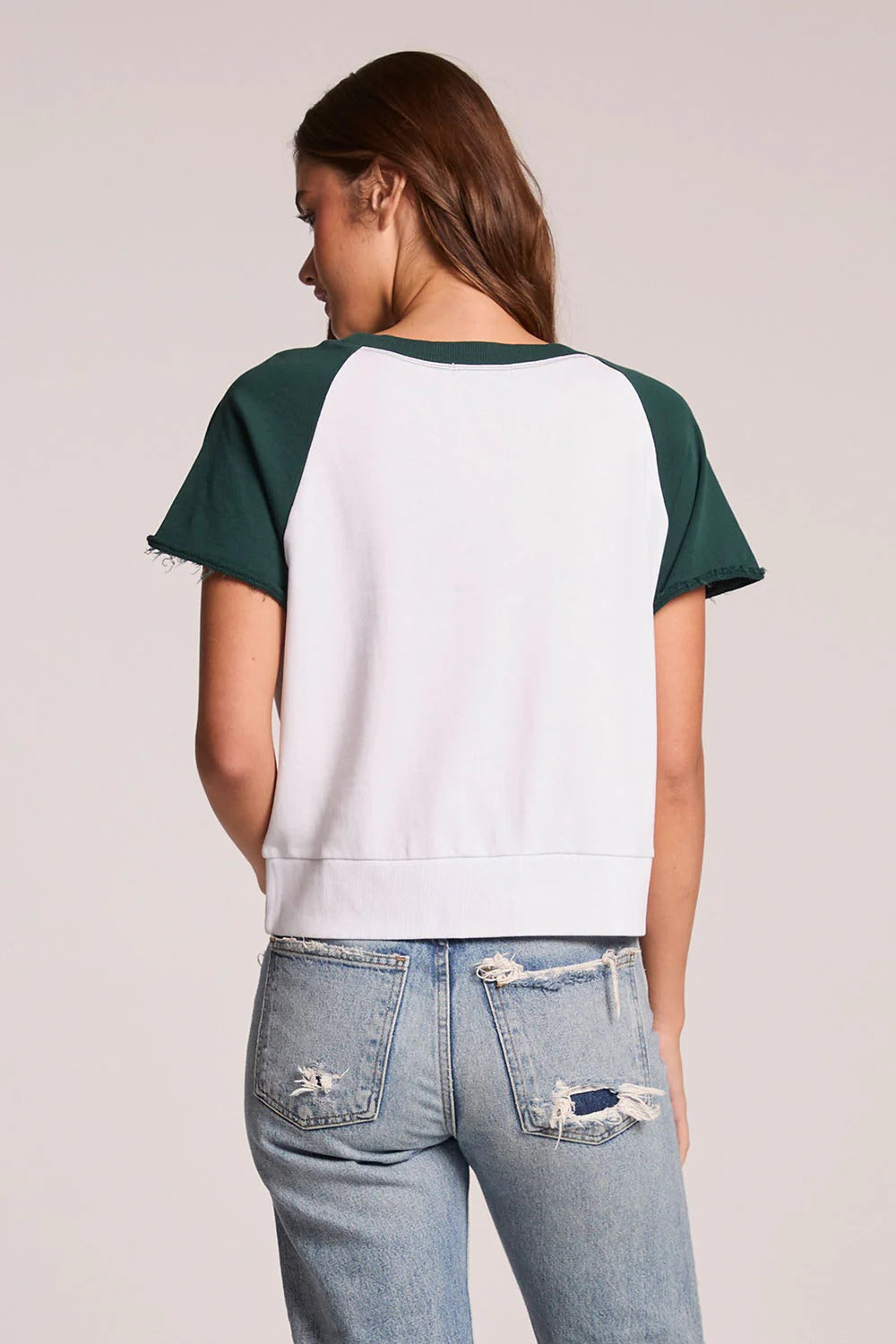 Person wearing a green and white baseball-style shirt with blue jeans on a plain background