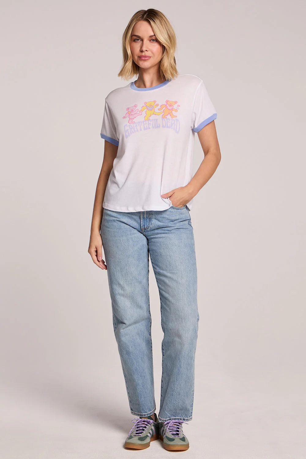 Woman wearing a white t-shirt with colorful graphics and blue jeans on a plain background