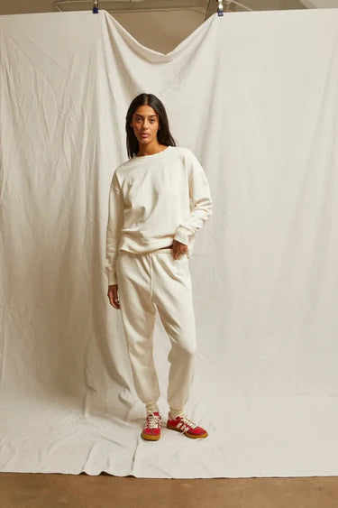 Person wearing a white outfit with red shoes standing against a plain white backdrop