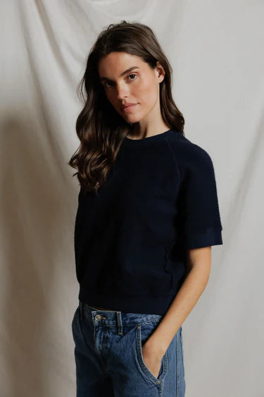Woman wearing a navy sweater and blue jeans against a plain background