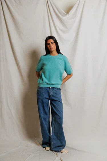 Person wearing a turquoise sweater and blue jeans against a plain background