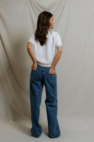Person wearing a white shirt and blue jeans against a plain background