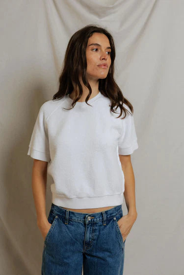 Woman wearing a white crop top and blue jeans against a plain background