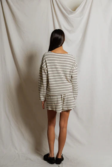 Person wearing a striped outfit standing against a plain white curtain