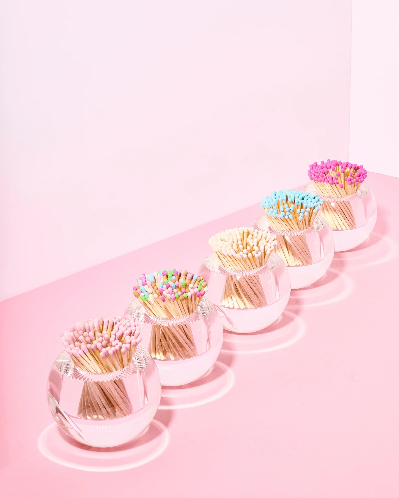 Clear glass holders with colorful matches on a pink background