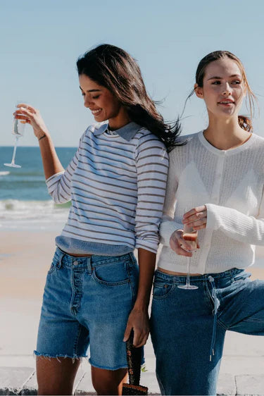 Two women standing on a beach, one holding a glass of wine.