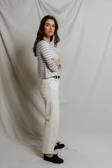 Woman wearing a striped shirt and white pants against a plain background