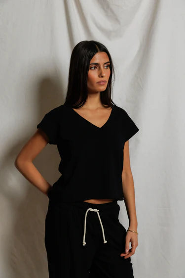 Woman wearing a black top and black pants with a white drawstring against a plain background