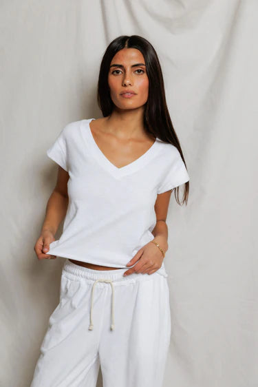 Woman wearing a white top and pants against a plain background