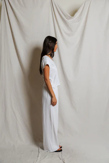 Woman in a white outfit standing against a plain white curtain