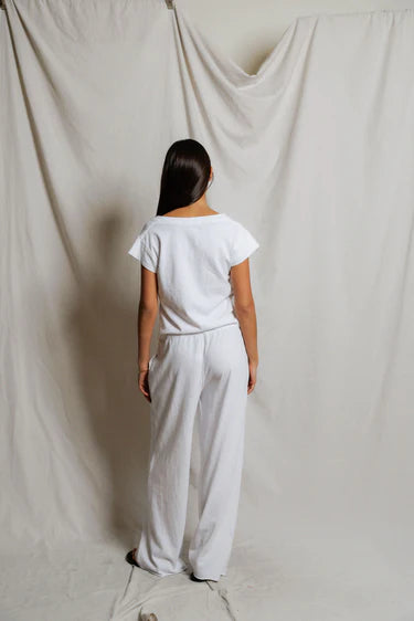Person wearing a white outfit standing against a plain white curtain