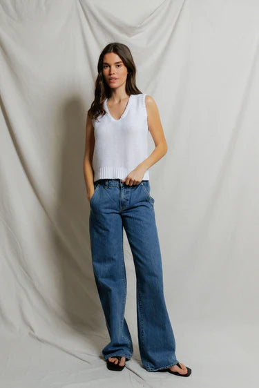Woman wearing a white sleeveless top and blue jeans against a plain background