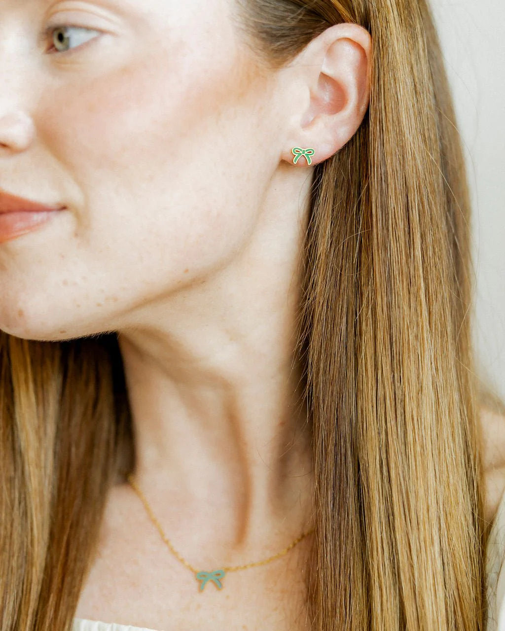 Close-up of a person wearing green bow-shaped earrings with a neutral background