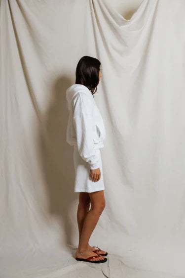 Person wearing a white hoodie standing in front of a draped white curtain