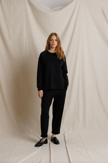 Person wearing a black outfit standing against a plain background