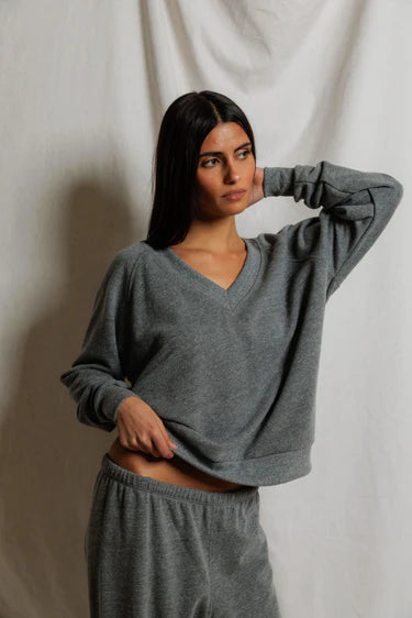 Woman wearing a gray sweater and pants against a plain background