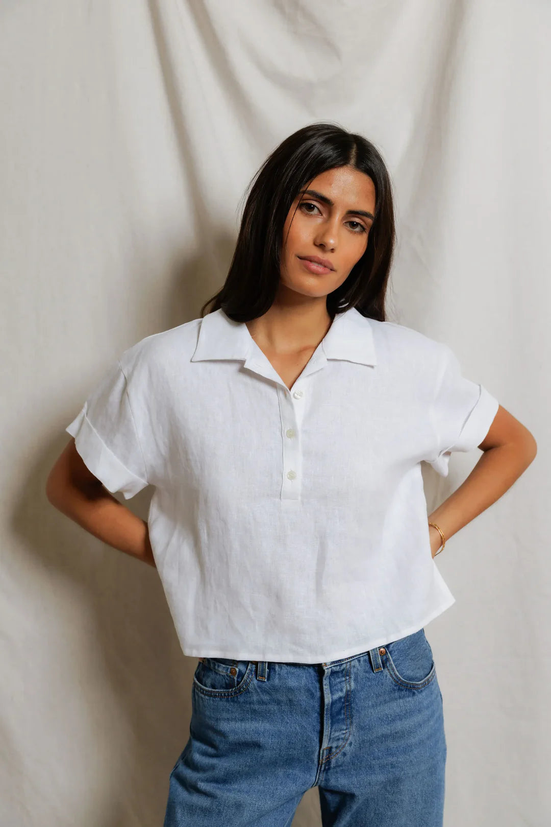 Woman wearing a white shirt and blue jeans against a plain background