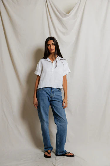 Woman wearing a white shirt and blue jeans standing against a plain background