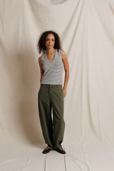 Woman wearing a striped tank top and green pants against a plain background