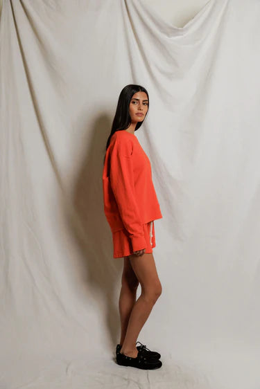 Person wearing a bright orange sweater and shorts against a plain white background