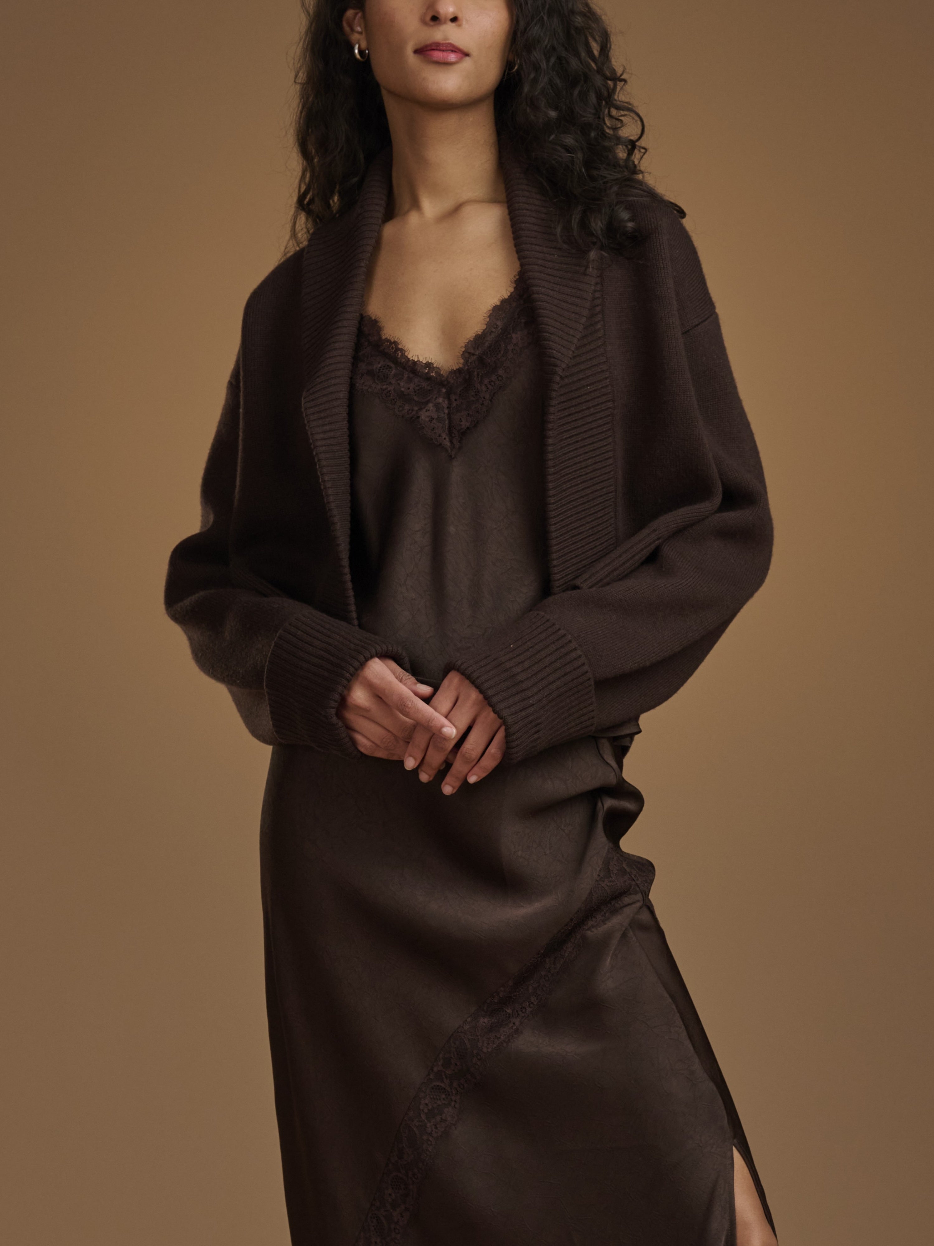 Woman wearing a dark brown dress with a matching cardigan against a brown background