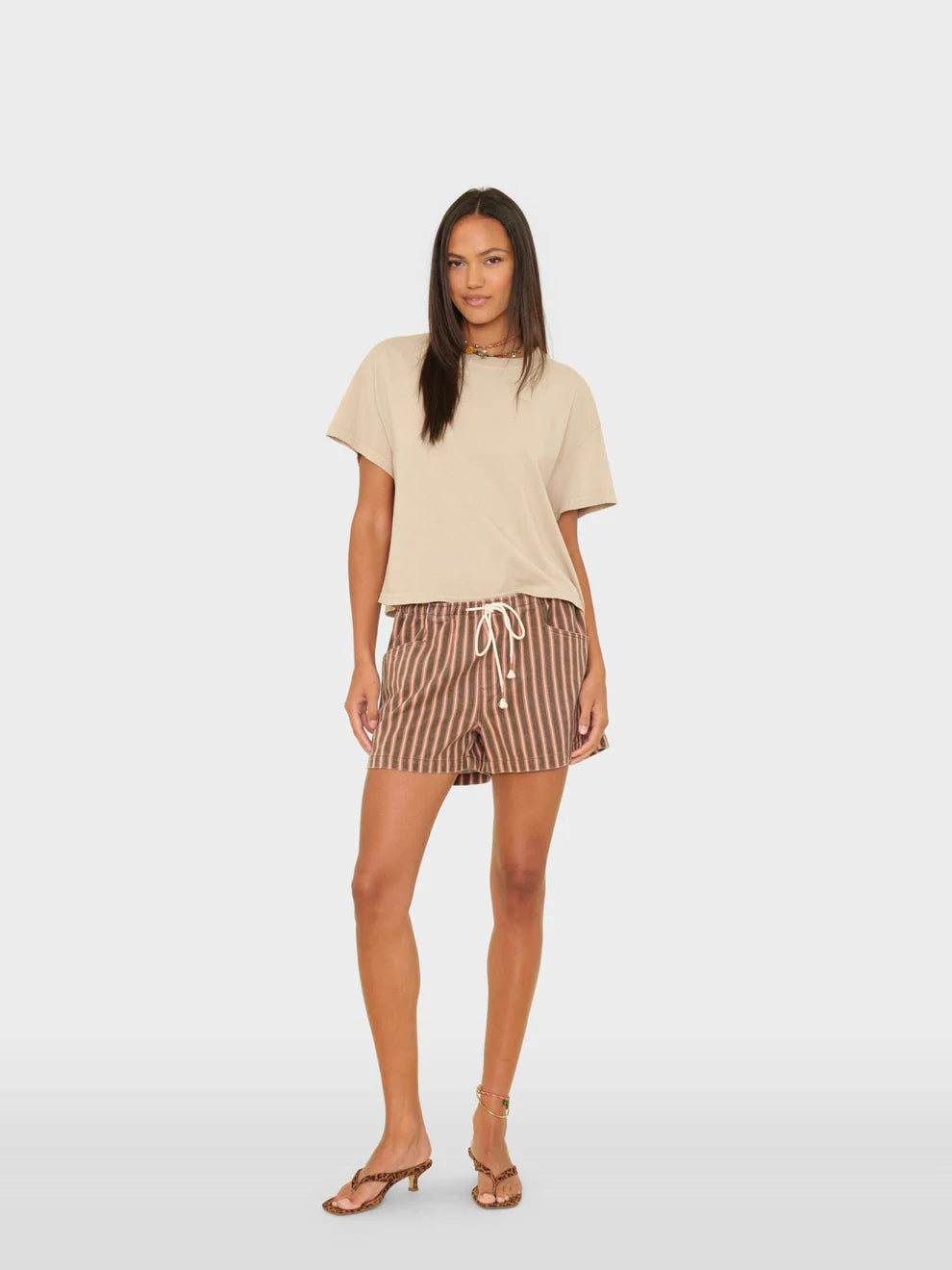 Woman wearing a beige top and striped shorts on a white background