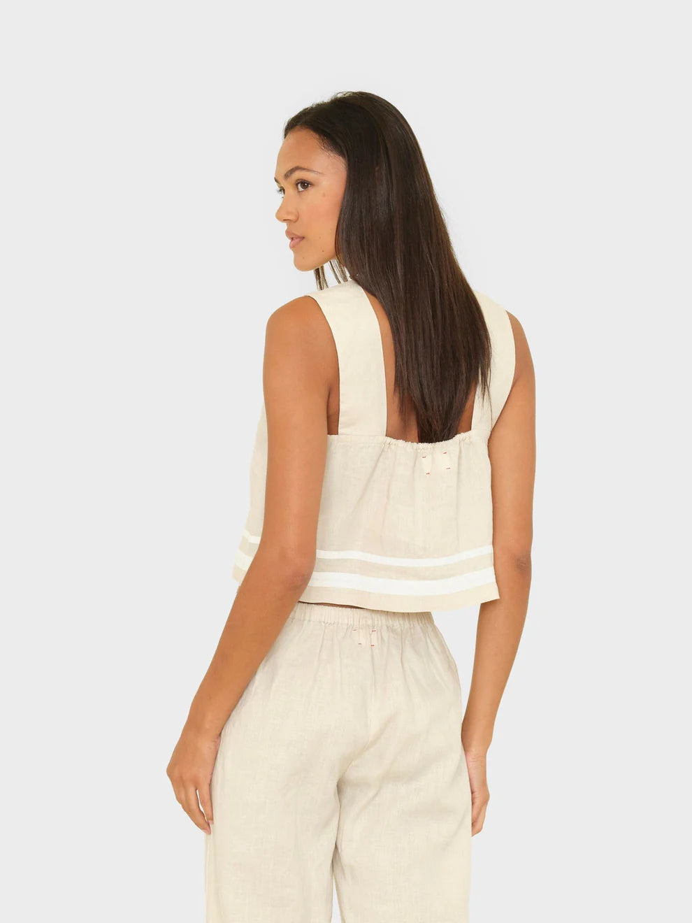 Woman wearing a sleeveless beige top and pants on a white background