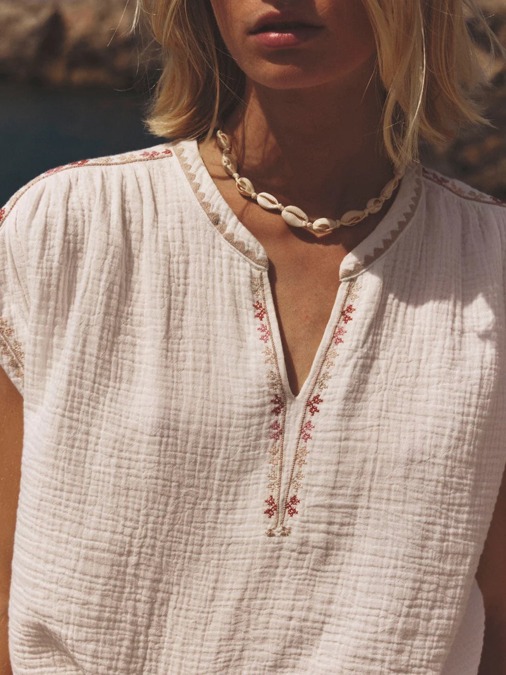 Close-up of a person wearing a white embroidered top with a necklace, blurred background