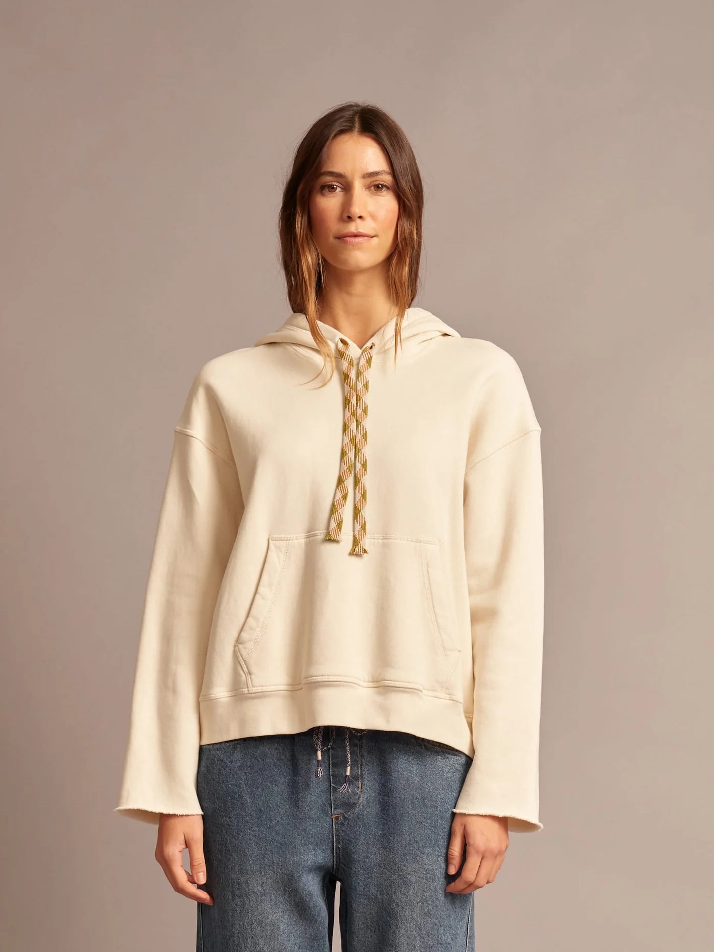 Woman wearing a beige hoodie with lace-up front on a plain background