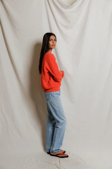 Person wearing a red sweater and blue jeans standing against a plain white background