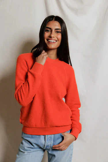 Woman wearing a bright orange sweater and light blue jeans against a plain background