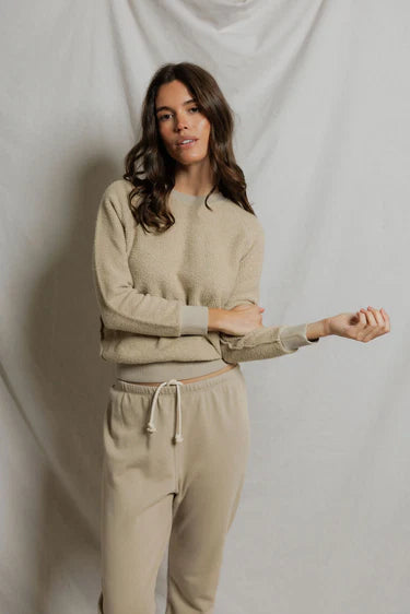 Woman wearing a beige sweater and pants against a plain background