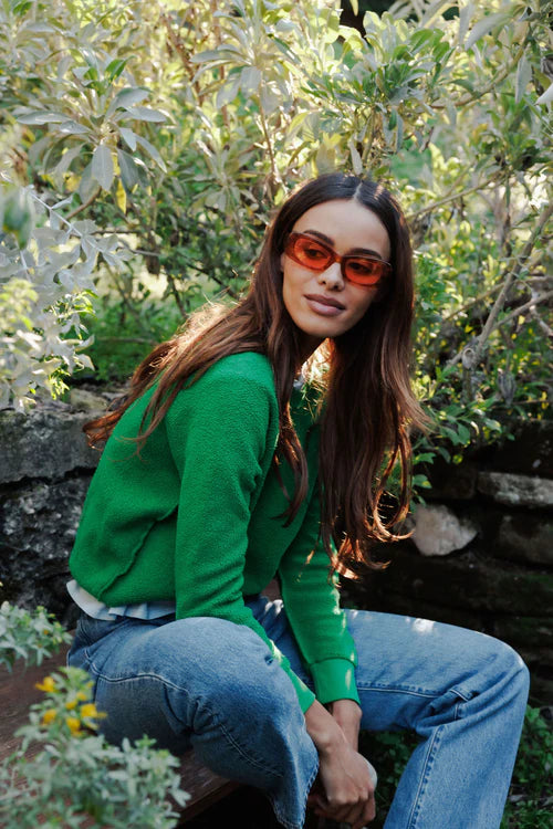 Woman wearing a green sweater and blue jeans sitting in a garden.