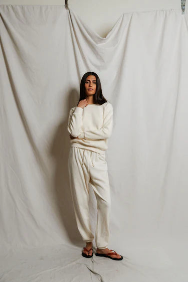 Person wearing a white outfit standing against a plain white curtain