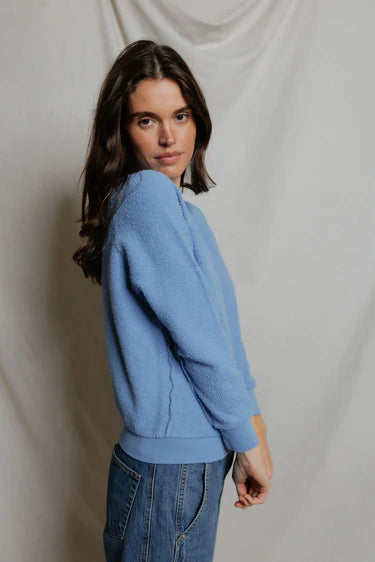 Woman wearing a blue sweater and jeans against a plain background