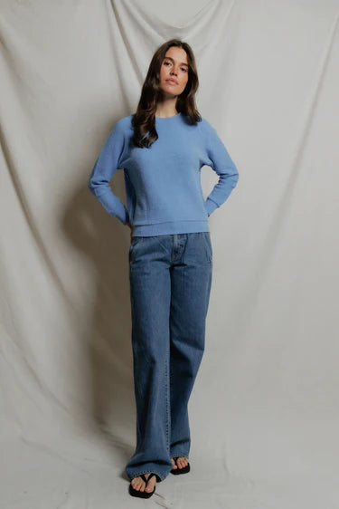 Woman wearing a blue sweater and jeans against a plain background