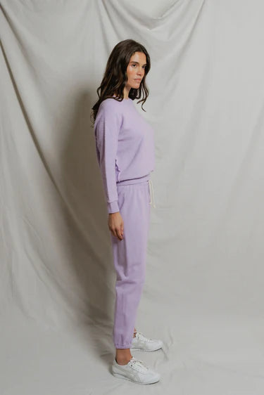 Woman wearing a lavender tracksuit against a plain background