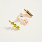 Two gold earrings with green and red gemstones on a light gray background