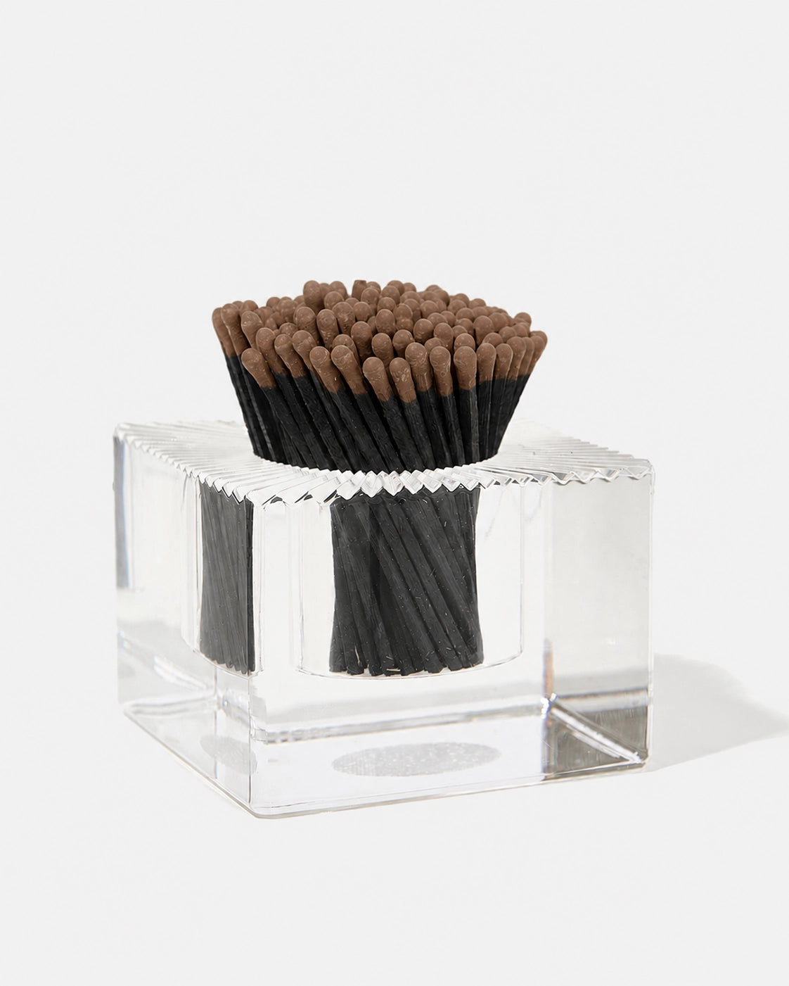 A set of black matchsticks with brown tips arranged inside a clear acrylic square container on a white background.