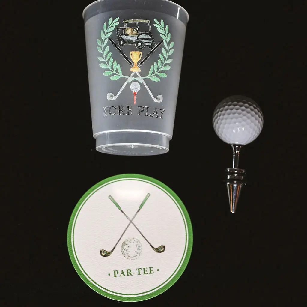 A golf-themed set featuring a frosted clear plastic cup with a graphic of a golf cart, laurel wreath, crossed golf clubs, a golf ball, and the words 'FORE PLAY'; a white wine bottle stopper shaped like a golf ball in a metal sleeve; and a round white coaster with green trim and crossed golf clubs reading 'PAR-TEE'.