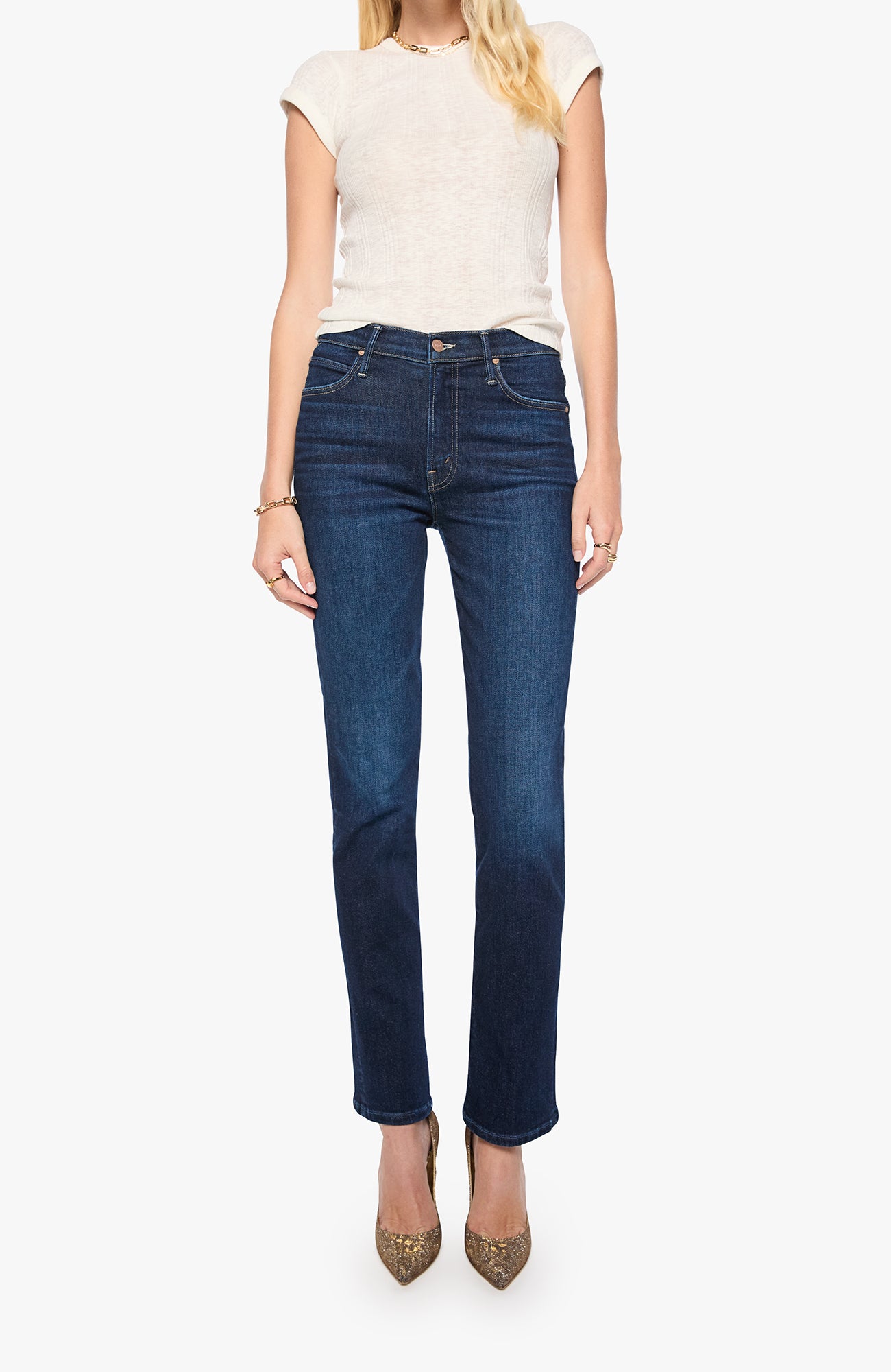 A model wearing dark blue straight-leg jeans, a cream short-sleeve knit top, and pointed-toe heels against a plain light gray background.