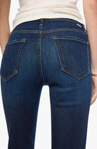 Close-up back view of a person wearing dark blue denim jeans with a cream top, showing the back pockets and waistband.