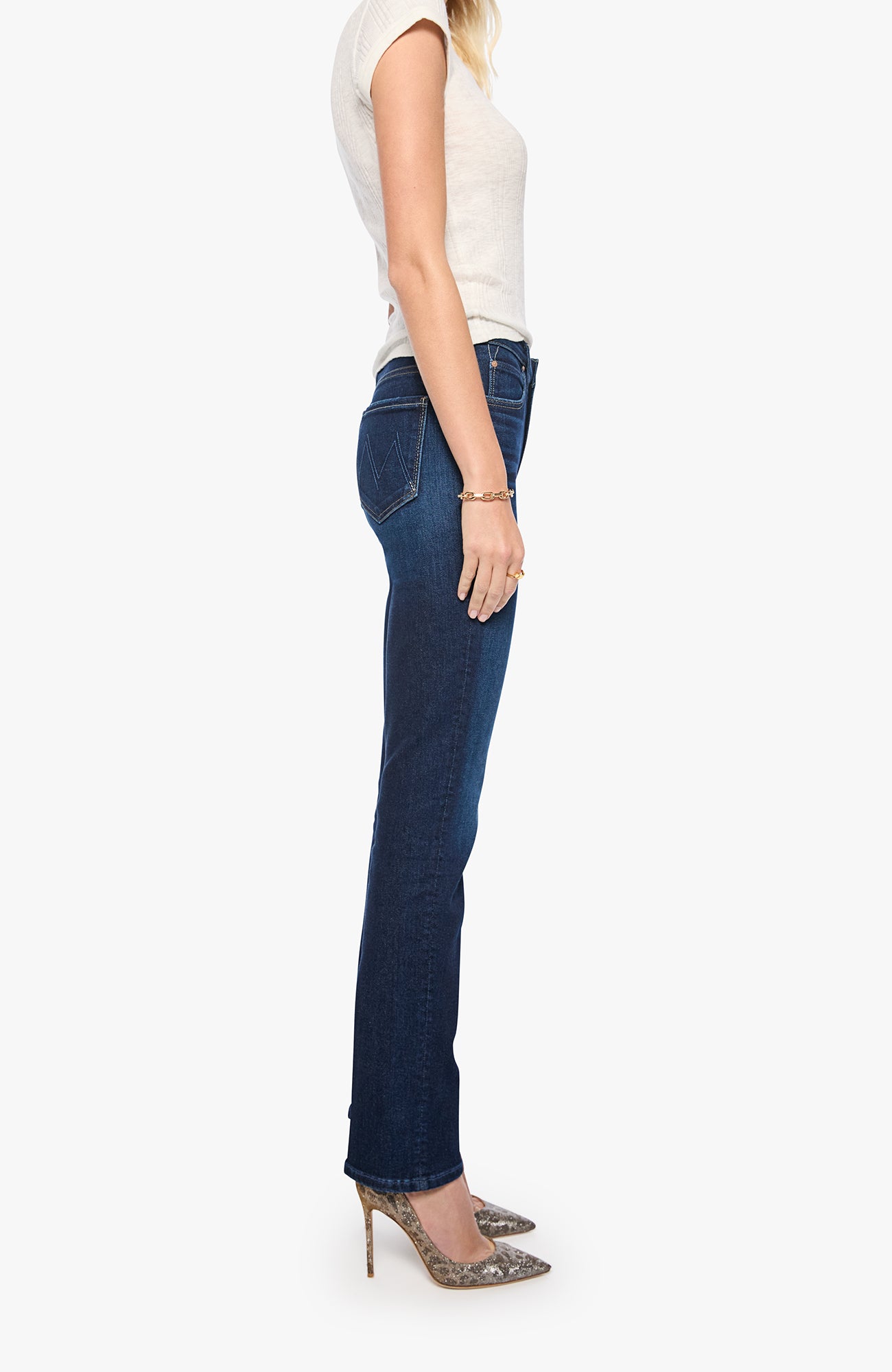 A side-profile view of a model wearing dark blue bootcut jeans, a white sleeveless top, and leopard-print high heels against a light gray background.