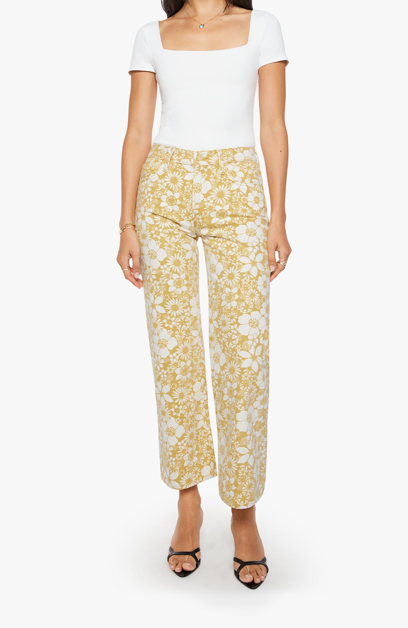 A model wearing high-waisted, wide-leg cropped trousers with a yellow and white floral pattern, paired with a white top and black strappy heels, against a plain white background.