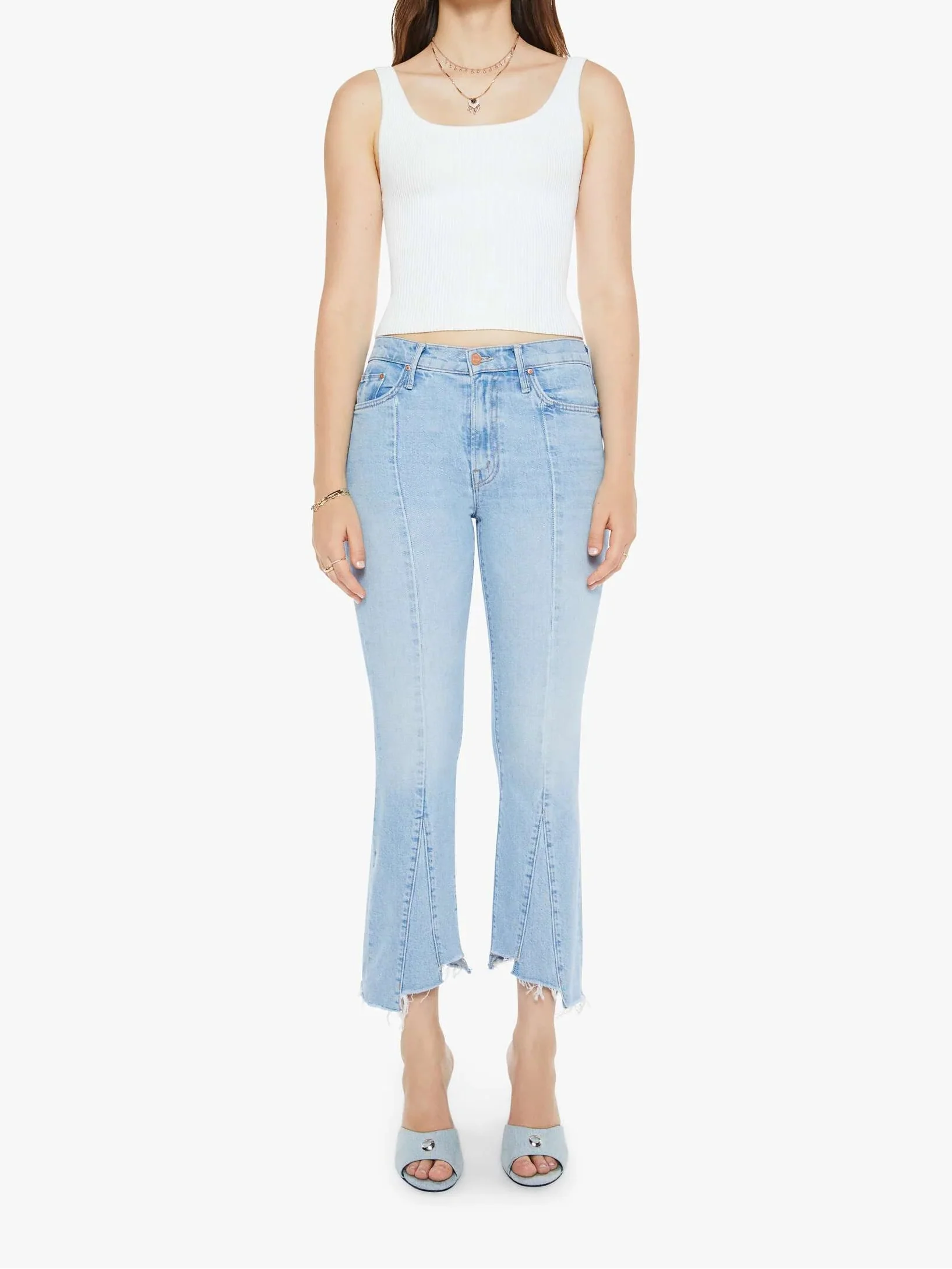 A woman standing straight, wearing a white tank top and light blue high-waisted bootcut jeans with a frayed hem.