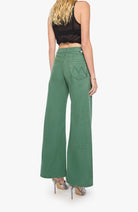A woman shown from the back wearing green wide-leg pants, a black sleeveless crop top, and metallic high-heeled sandals against a light gray studio background.