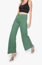 A model wearing a pair of green wide-leg cropped jeans with a black crop top and metallic gray heels, shown from the waist down against a plain white background.