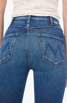 Close-up back view of a person wearing blue denim jeans with a cream ribbed top, showing the back pockets and waistband details.