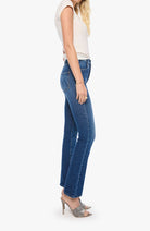 A side-profile view of a model wearing blue high-rise flare jeans, a cream sleeveless top, and gray heeled sandals against a plain white background.